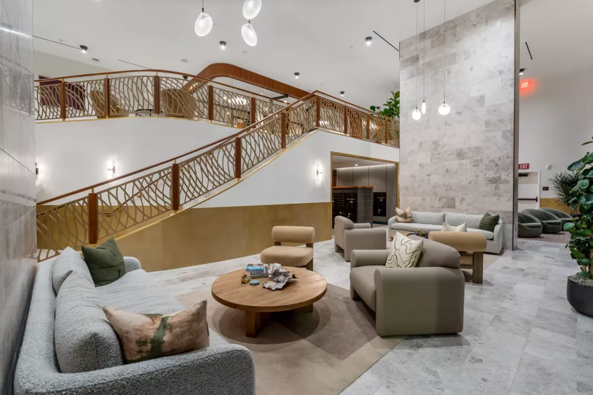 Modern lobby with curved staircase, neutral seating, and decorative wood and brass railing.