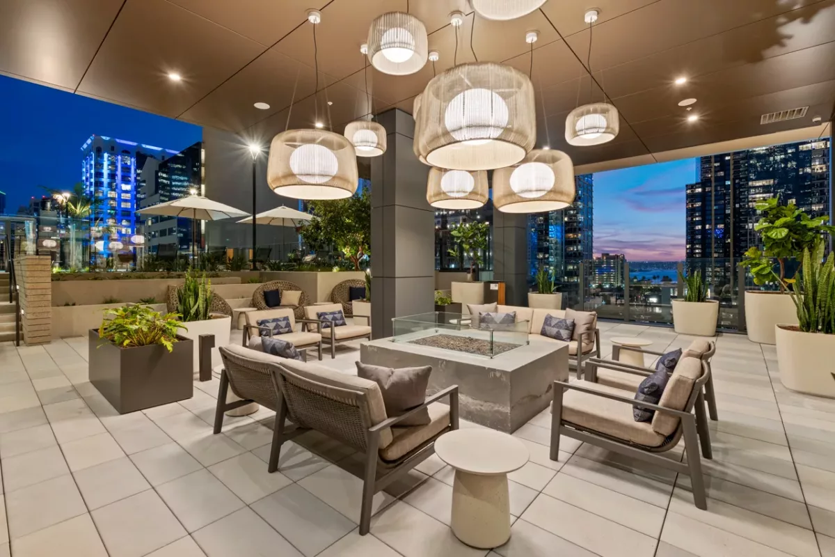 Modern rooftop lounge with cushioned seating, fire pit, and city skyline at dusk.