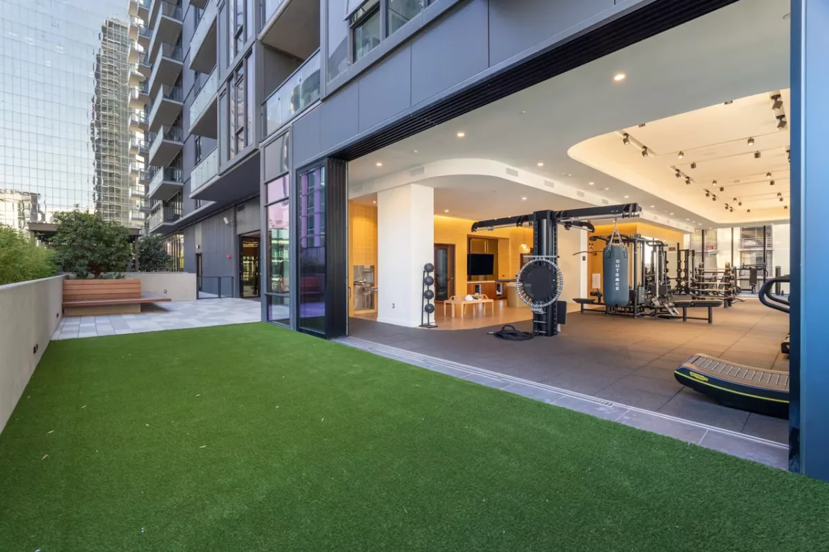 Indoor-outdoor fitness center with turf lawn, strength equipment, and open glass doors.