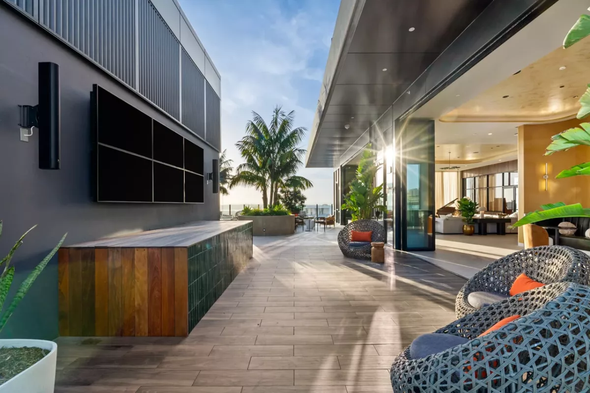 Outdoor lounge with woven chairs, palm trees, and wall-mounted theater screens at sunset.