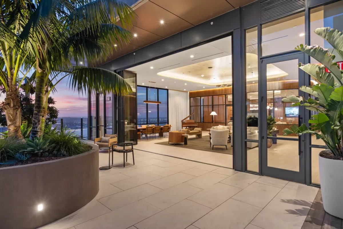 Open-air terrace with palm trees and lounge seating overlooking sky lounge interior at sunset.
