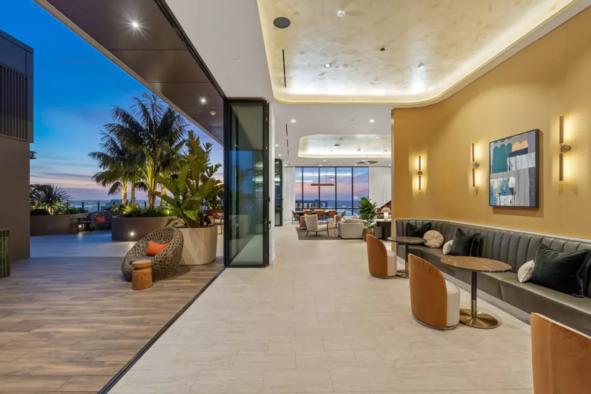 Indoor lounge opens to terrace with palm trees, cozy seating, and sunset sky in the background.