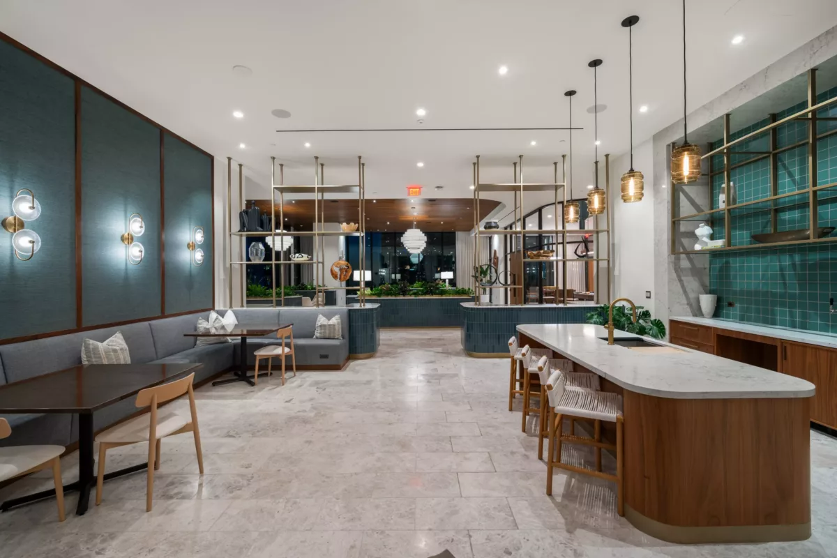 Clubroom at dusk with marble island, booth seating, pendant lights, and open shelving.