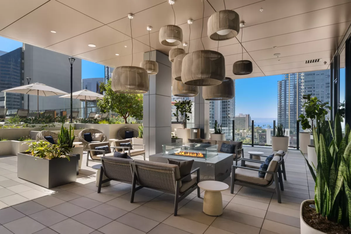 Outdoor lounge with firepit, modern seating, pendant lights, and city skyline view.