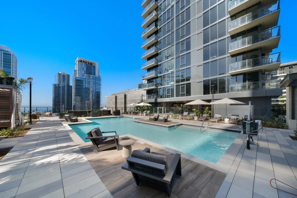 Modern rooftop pool with lounge chairs, umbrellas, and city skyline in the background.

