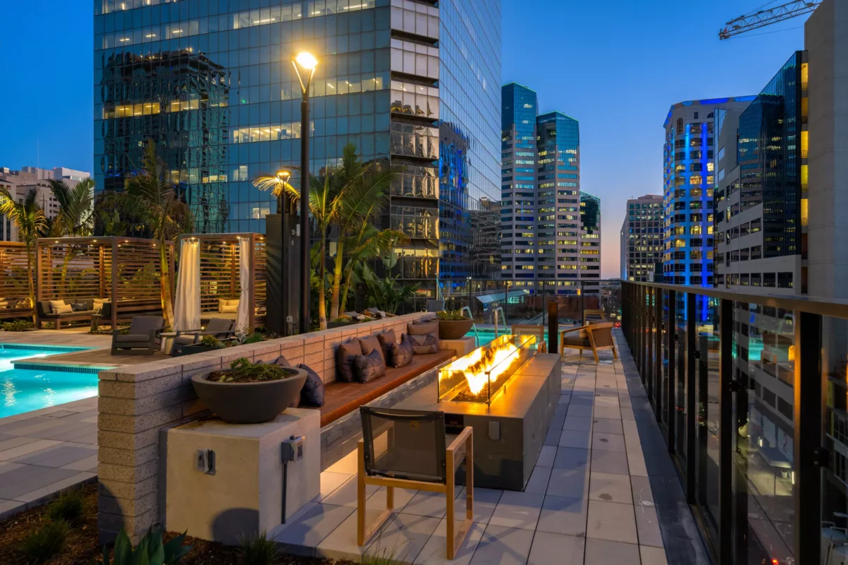Rooftop fire pit lounge by pool with city skyscrapers and glass rail at dusk.
