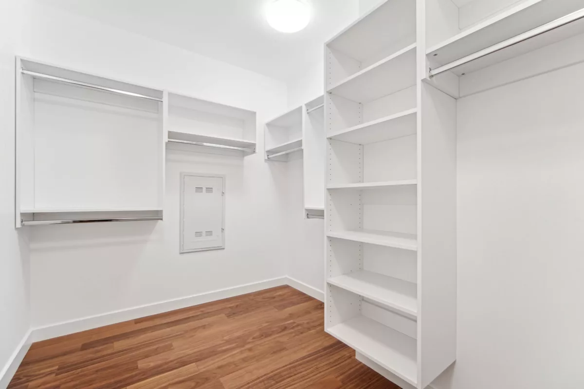 Spacious closet with white shelving, hanging rods, and hardwood floors under bright lighting.