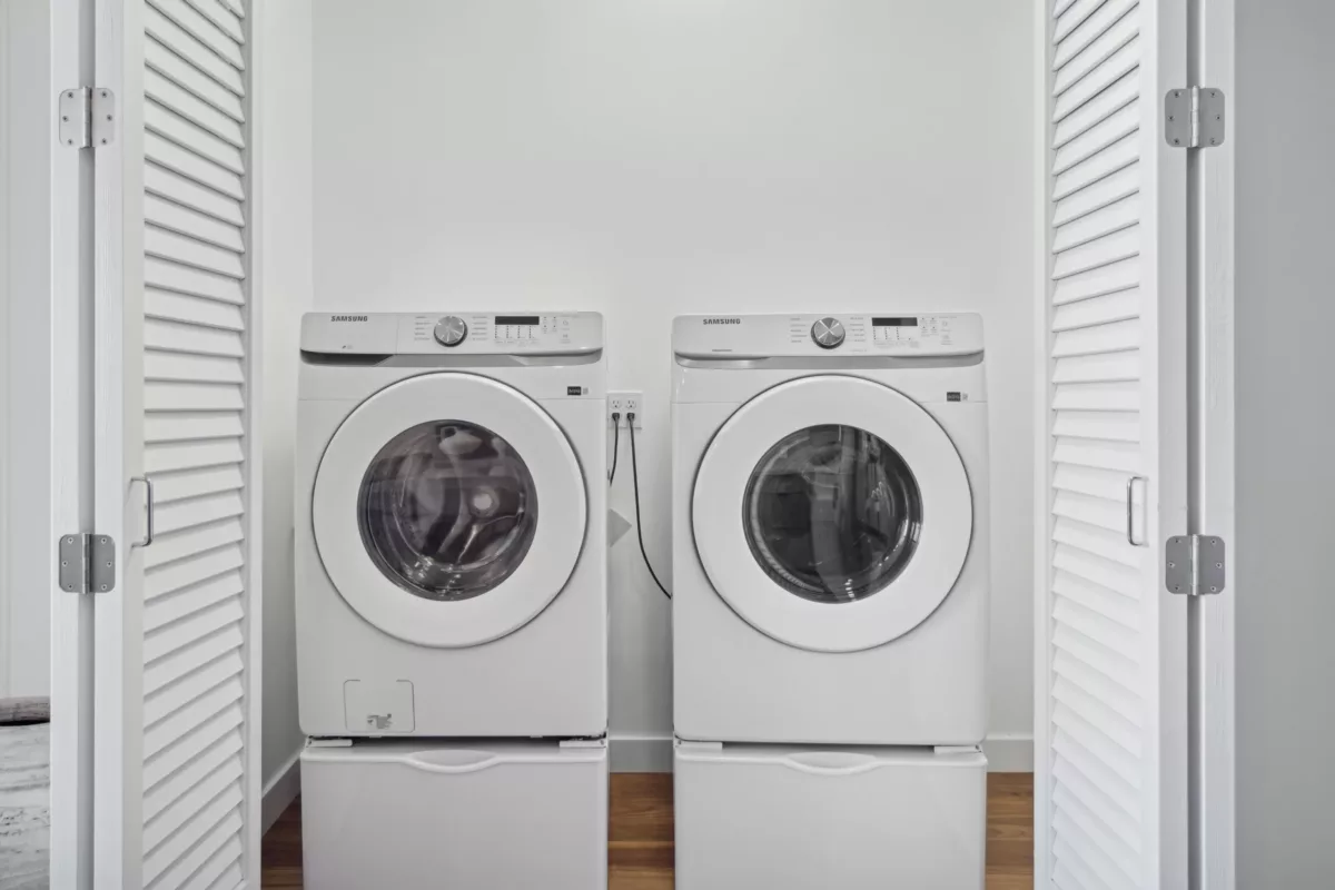 Laundry closet with front-loading washer and dryer enclosed by white louvered doors.