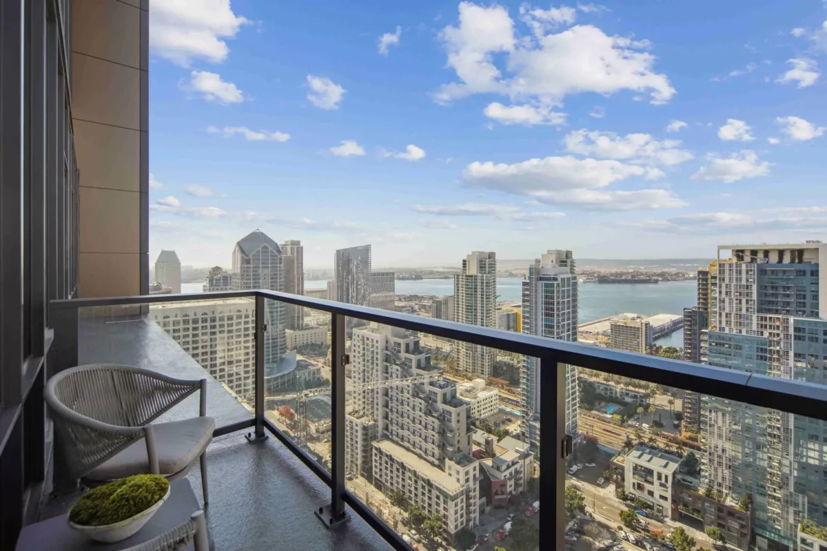 Outdoor balcony with glass railing, modern seating, and panoramic views of the city and waterfront.