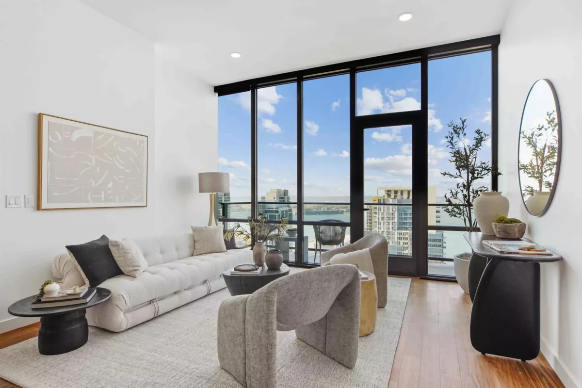 Contemporary living room featuring neutral tones, with a white sofa, modern chairs, and large windows overlooking a city and water view.