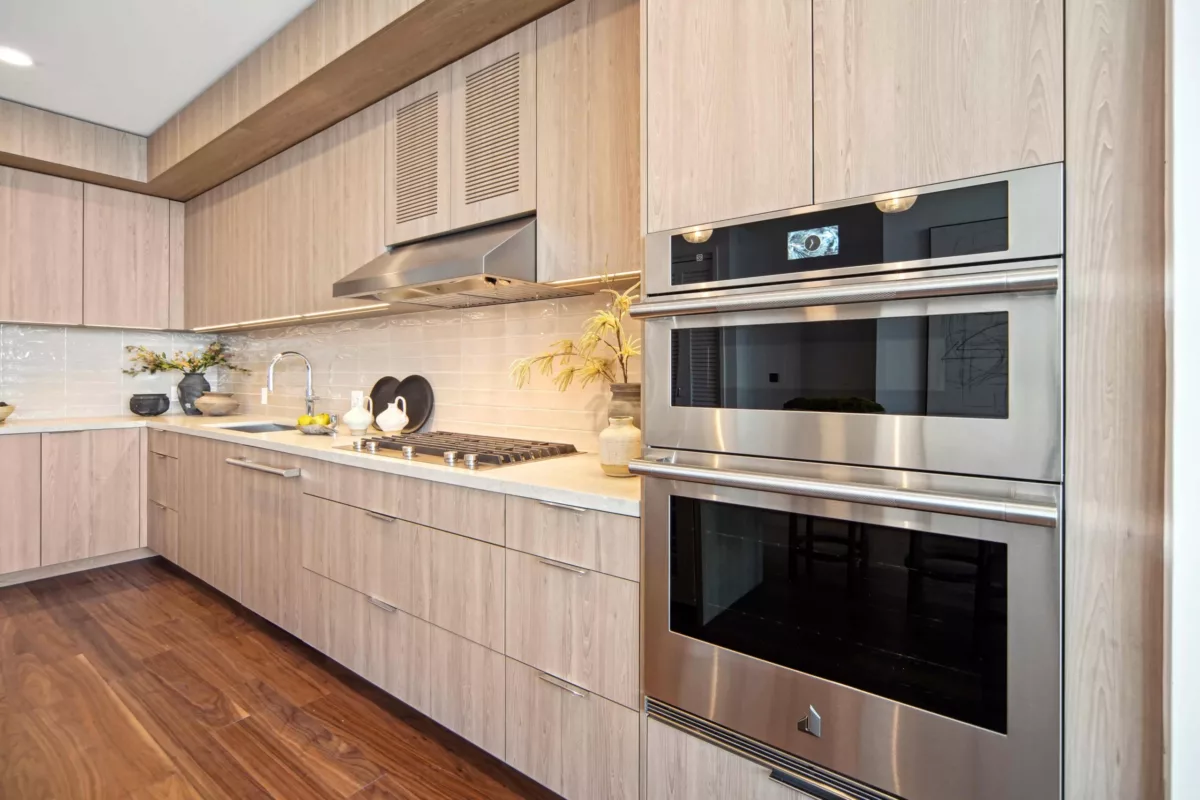 Sleek kitchen with light wood -style cabinetry, dstacked oven and microwave, and a modern cooktop, accented by neutral backsplash and minimalist decor.