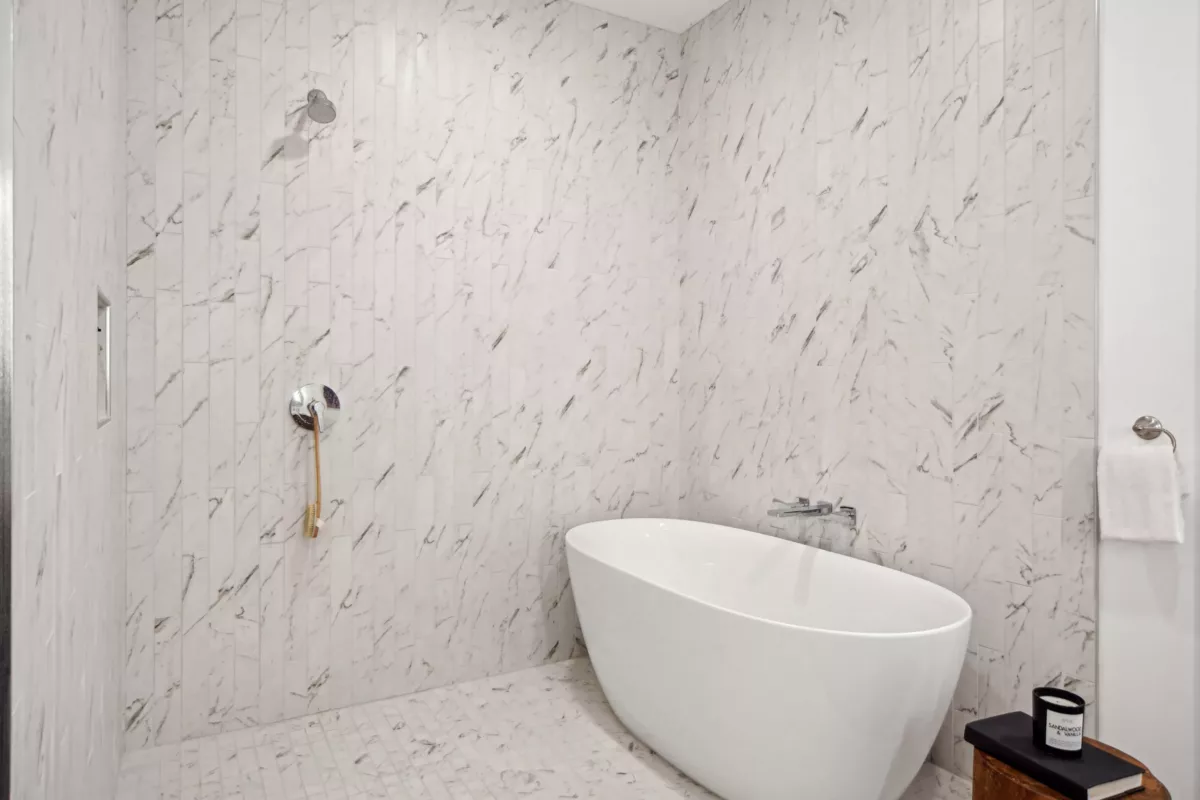 Freestanding white bathtub against a marble-tiled wall, accompanied by minimalist decor and neutral tones.