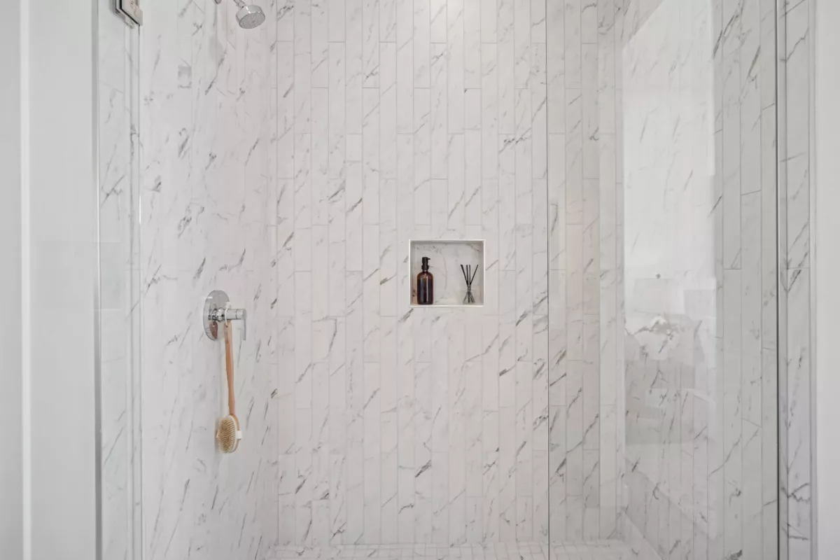 Close-up of a marble shower with a built-in niche holding toiletries and a wall-mounted showerhead.