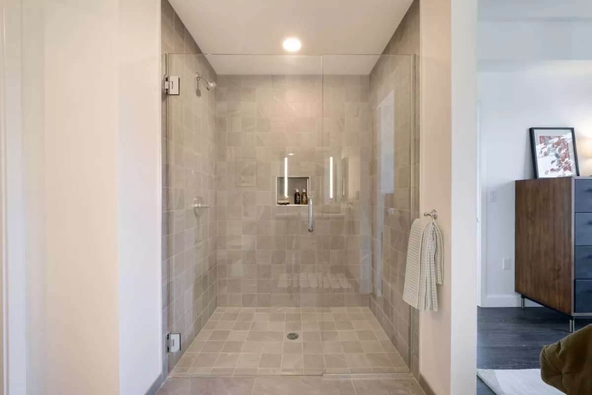 Spacious shower with gray tile walls, glass door, and a built-in niche for toiletries.