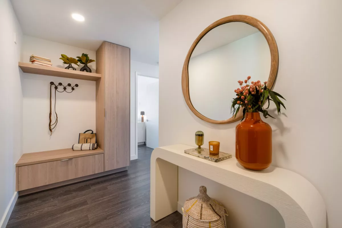 Entryway with a curved console table, round mirror, and wood storage bench with hooks and shelves.
