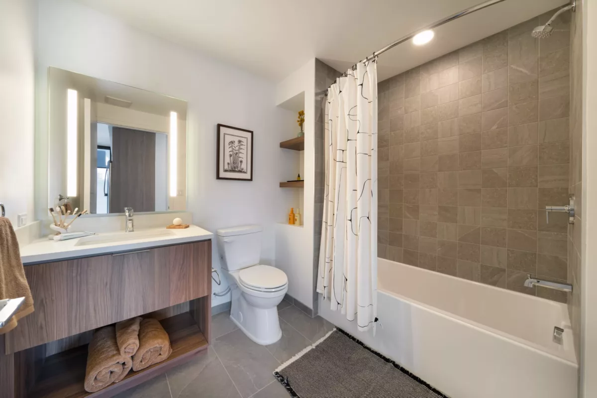 Modern bathroom with a wood vanity, large mirror, toilet, shower, and an open closet with shelves.