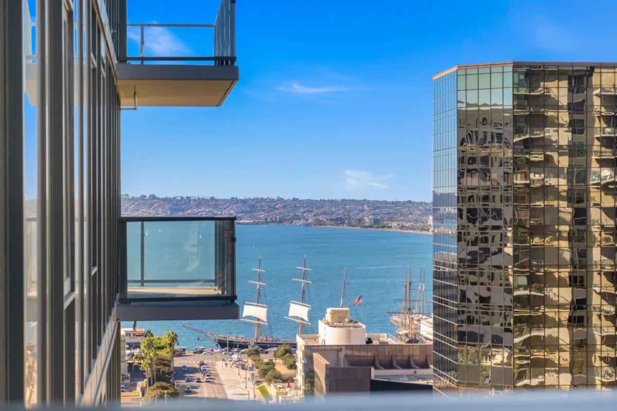 Balcony view of a harbor with sailing ships, framed by modern glass buildings and balconies.