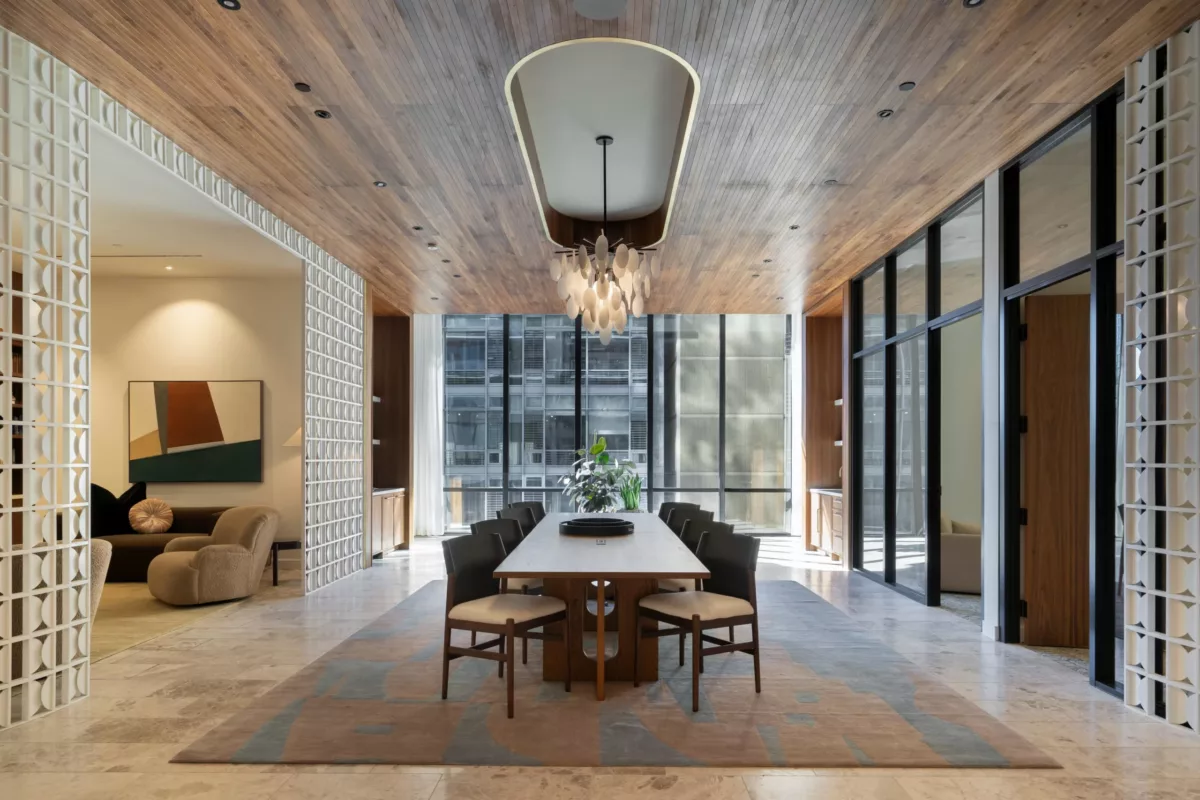 Elegant meeting space with a long wooden table, modern chairs, large windows, a wood-paneled ceiling, and a central chandelier.