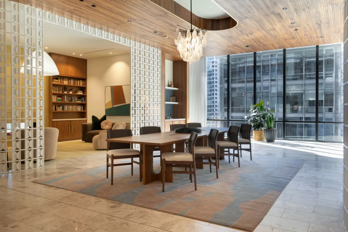 Elegant meeting space with a long wooden table, modern chairs, large windows, a wood-paneled ceiling, and a central chandelier.