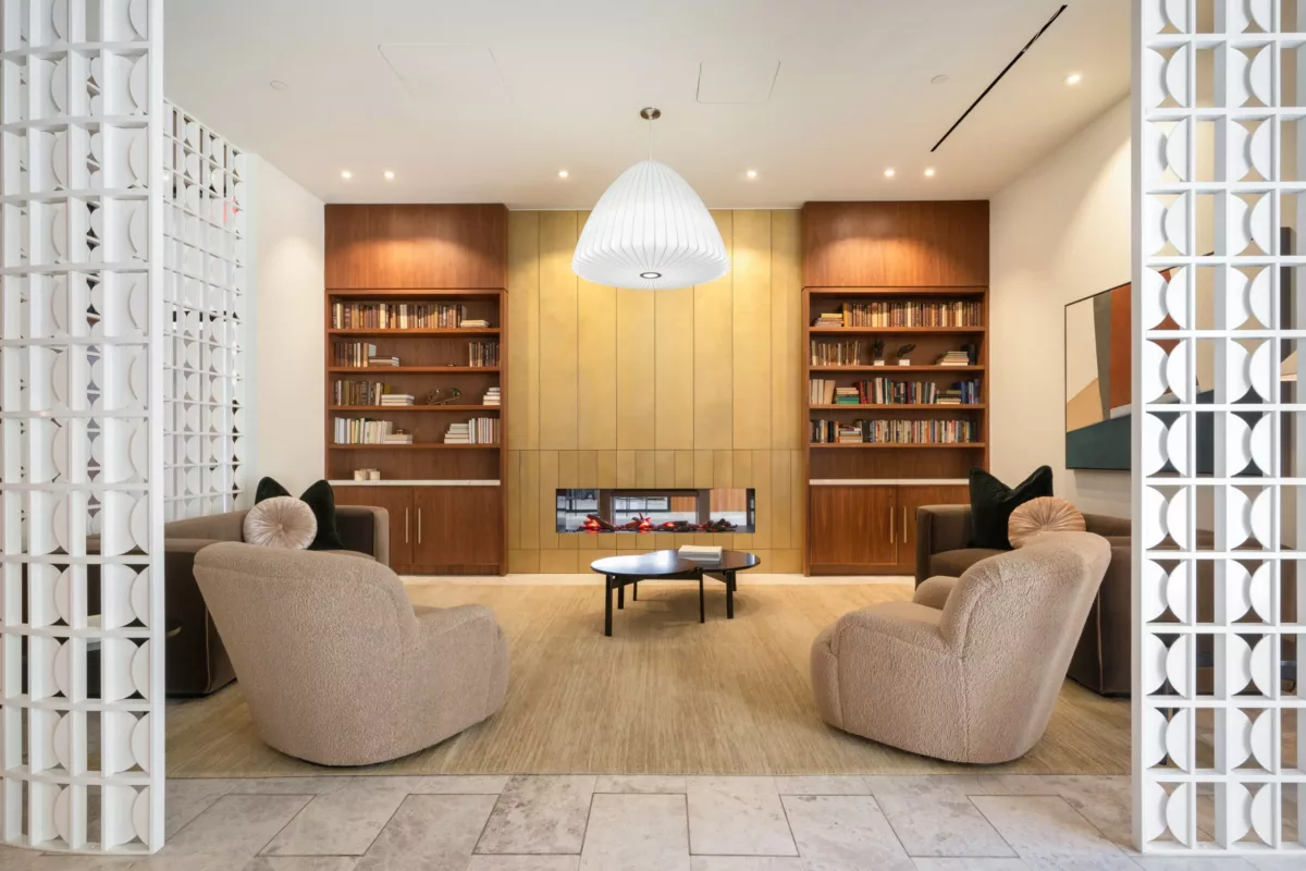 Library lounge featuring built-in bookshelves, beige armchairs, a modern fireplace, and a large pendant light in a cozy seating area.
