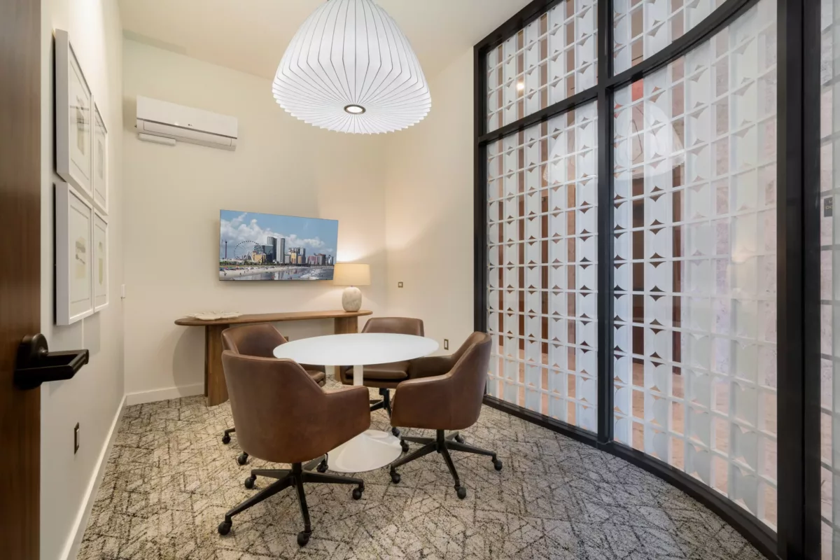 Private meeting room with a round table, leather chairs, a large pendant light, and glass walls with geometric patterns.