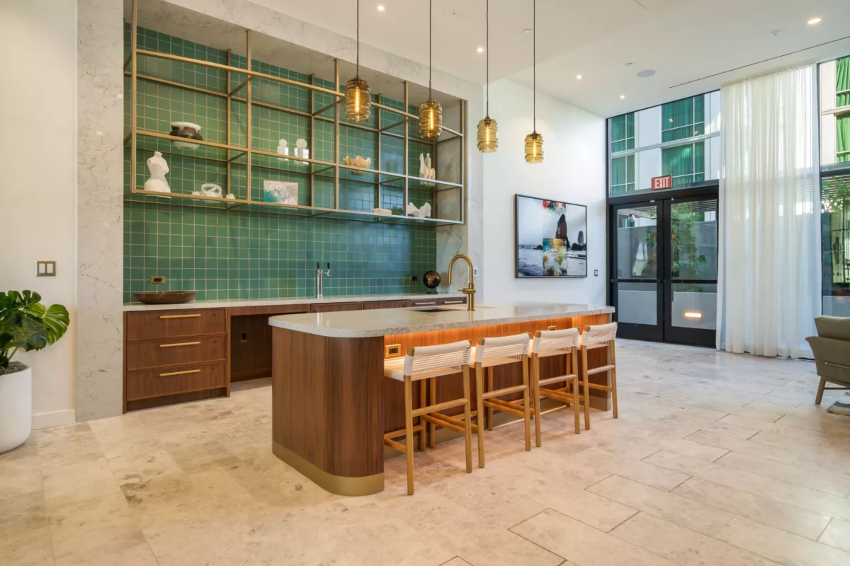 Open kitchen area with green-tiled walls, a marble island with wooden accents, pendant lighting, and seating for four.