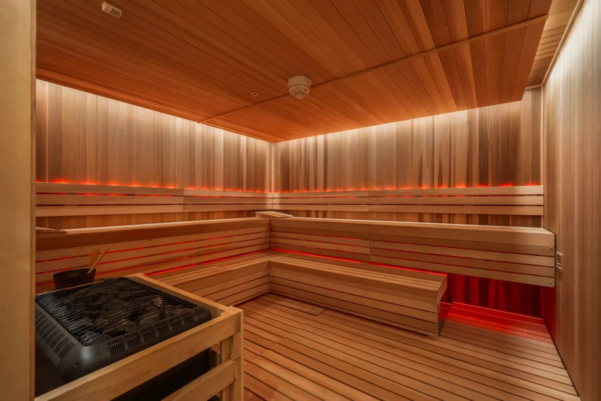 Wooden sauna interior with bench seating, warm lighting, and a heater unit.