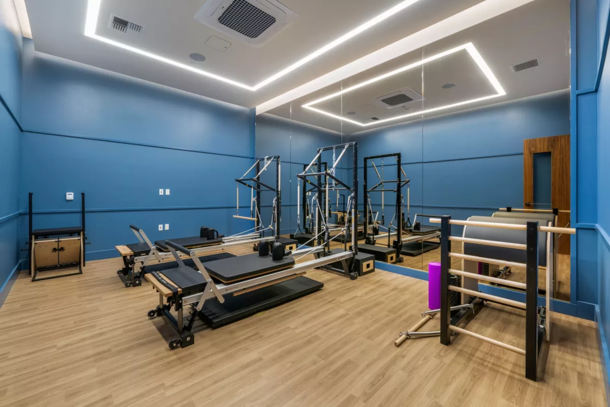 Pilates studio with blue walls, mirror, reformer machines, barre, and wood flooring.