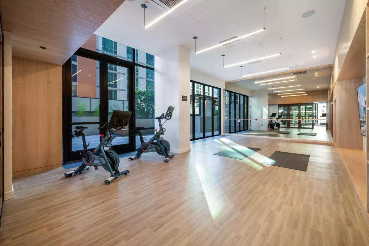 Bright fitness room with stationary bikes, yoga mats, mirrors, and floor-to-ceiling windows.