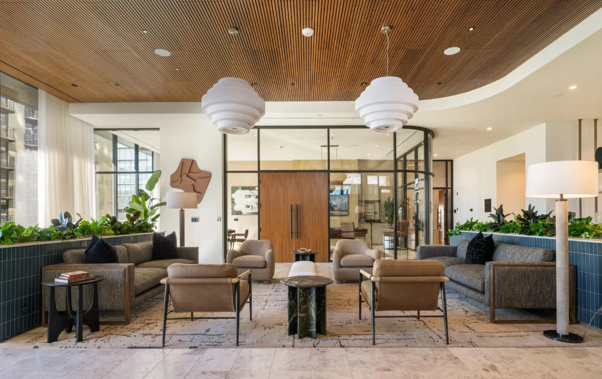 Chic lounge with mixed seating, wooden ceiling, greenery accents, and large glass doors leading to additional spaces.