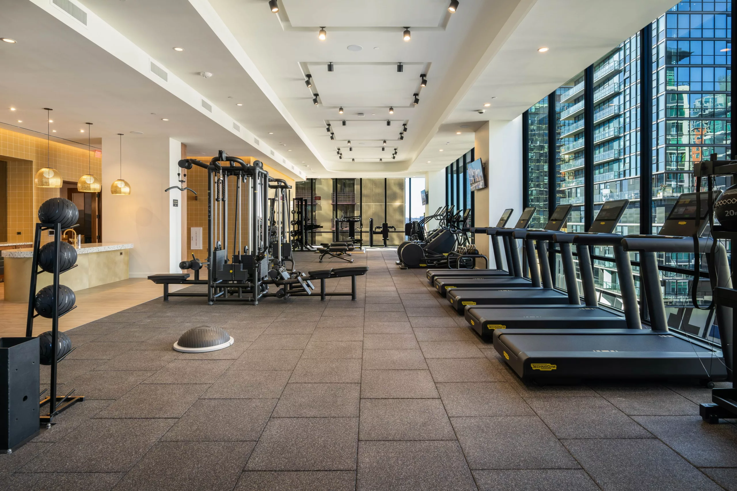 Spacious gym with treadmills, weight machines, and floor-to-ceiling windows overlooking the city.