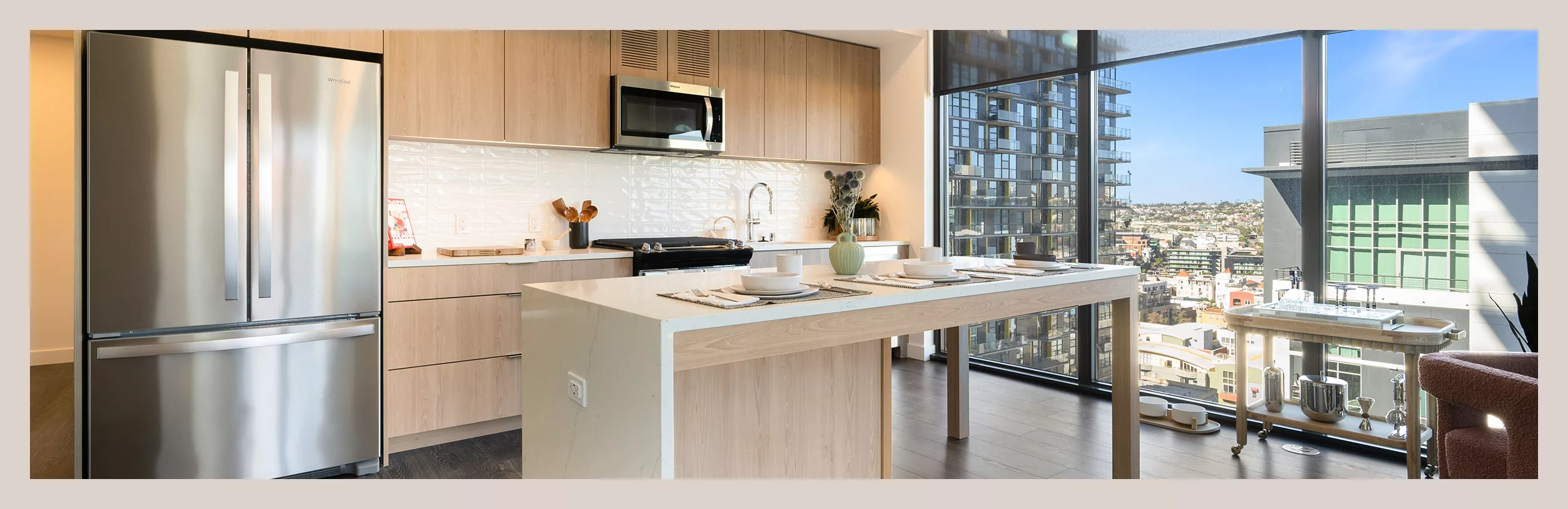 Kitchen with light wood-style cabinets, stainless steel appliances, center island, and floor-to-ceiling windows overlooking a city.