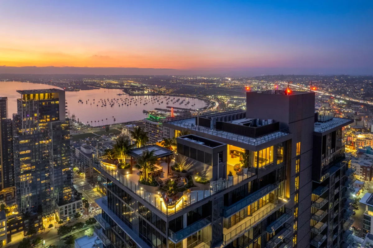 Aerial view of rooftop lounge and city skyline at dusk with marina and glowing lights below.